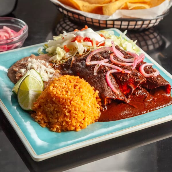 Three enchiladas with red sauce, rice, refried beans, and lime wedges on a blue plate.