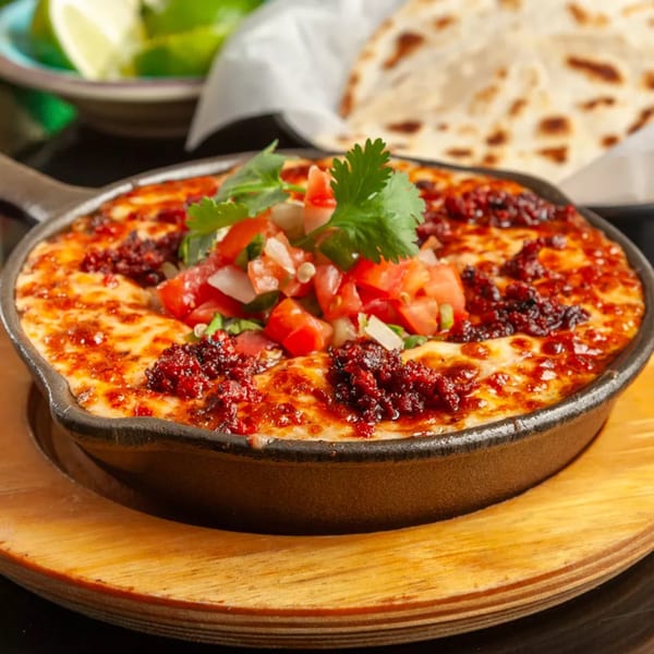 Melted cheese with chorizo and pico de gallo in a cast iron skillet, with tortillas and limes.
