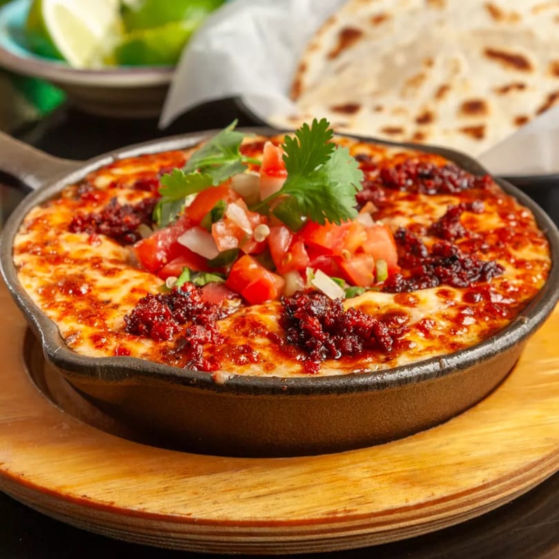 Melted cheese with chorizo and pico de gallo in a cast iron skillet, with tortillas and limes.