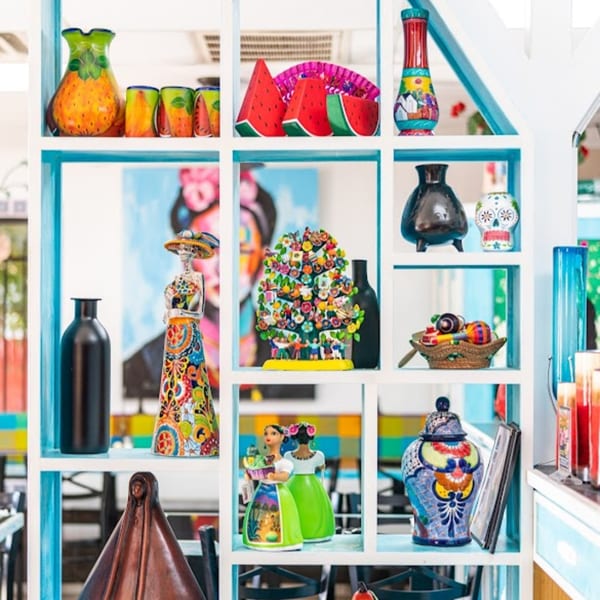A white and blue shelving unit filled with colorful Mexican pottery, figurines, and decor.