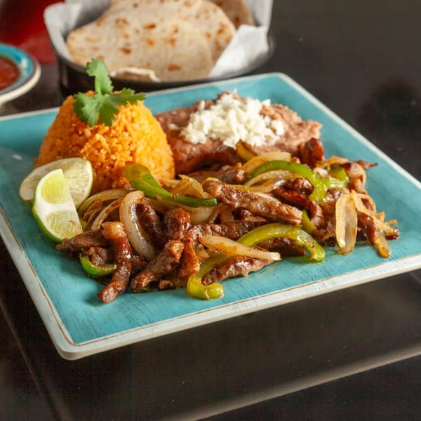 Sizzling beef fajitas with bell peppers and onions, served with rice, beans, and tortillas.