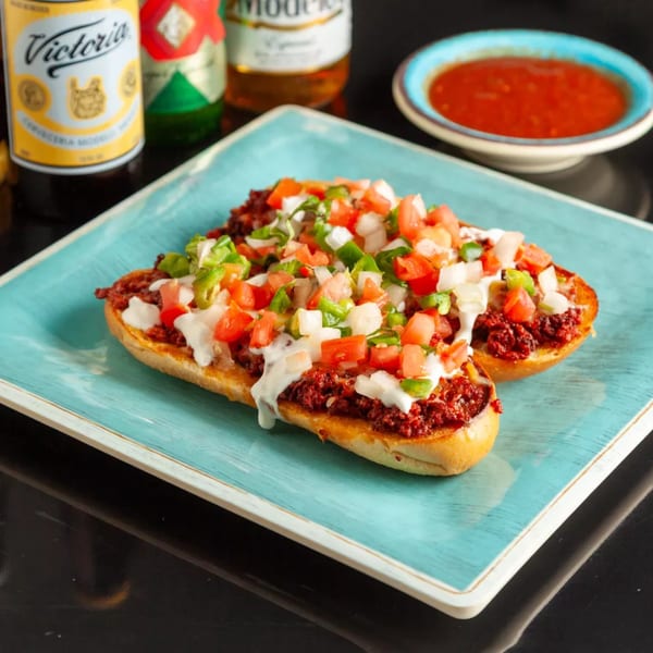 Two Mexican bolillos topped with chorizo, pico de gallo, and crema on a blue plate.