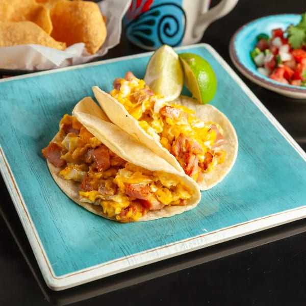 Two breakfast tacos filled with scrambled eggs and ham, garnished with lime wedges on a blue plate.