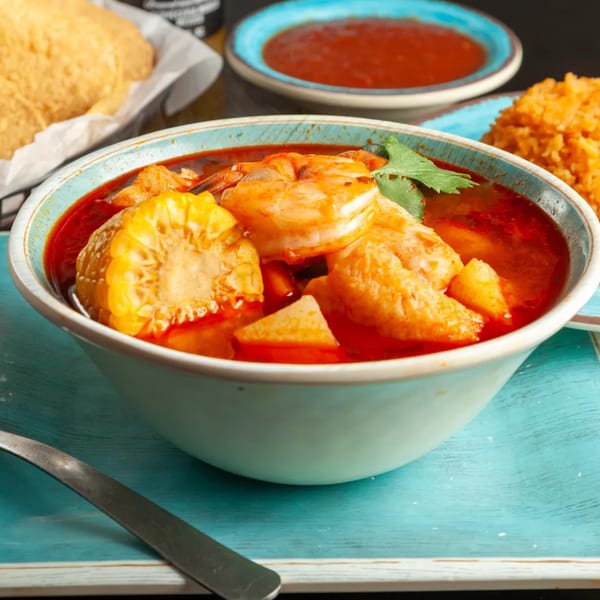 Shrimp soup with corn on the cob, cilantro, and red broth, served with rice and chips.