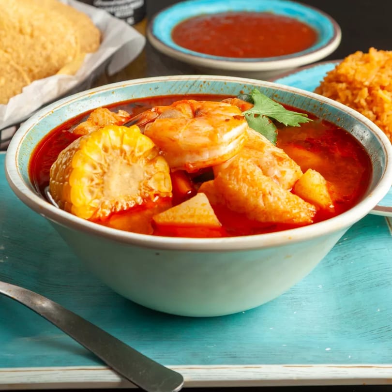 Shrimp soup with corn on the cob, cilantro, and red broth, served with rice and chips.