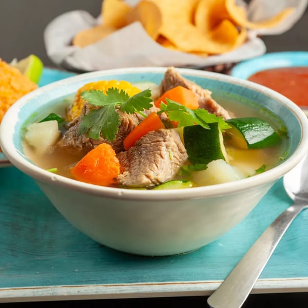 Hearty beef soup with corn, carrots, zucchini, and cilantro, served with chips and salsa.