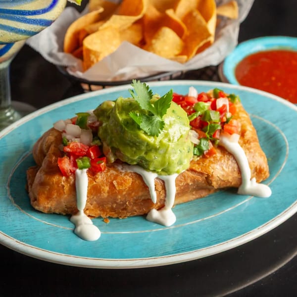 Golden-brown chimichanga topped with guacamole, pico de gallo, and sour cream on a blue plate.