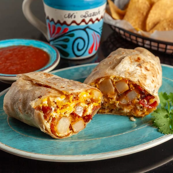 Two halves of a breakfast burrito filled with eggs, potatoes, and bacon on a blue plate.