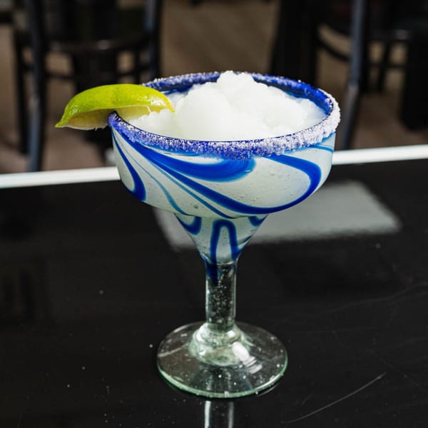 Frozen margarita in a blue and white swirled glass with a salted rim and lime wedge.