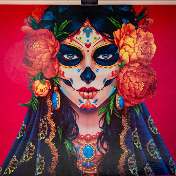 Colorful painting of a woman with Day of the Dead sugar skull makeup and flowers in her hair.